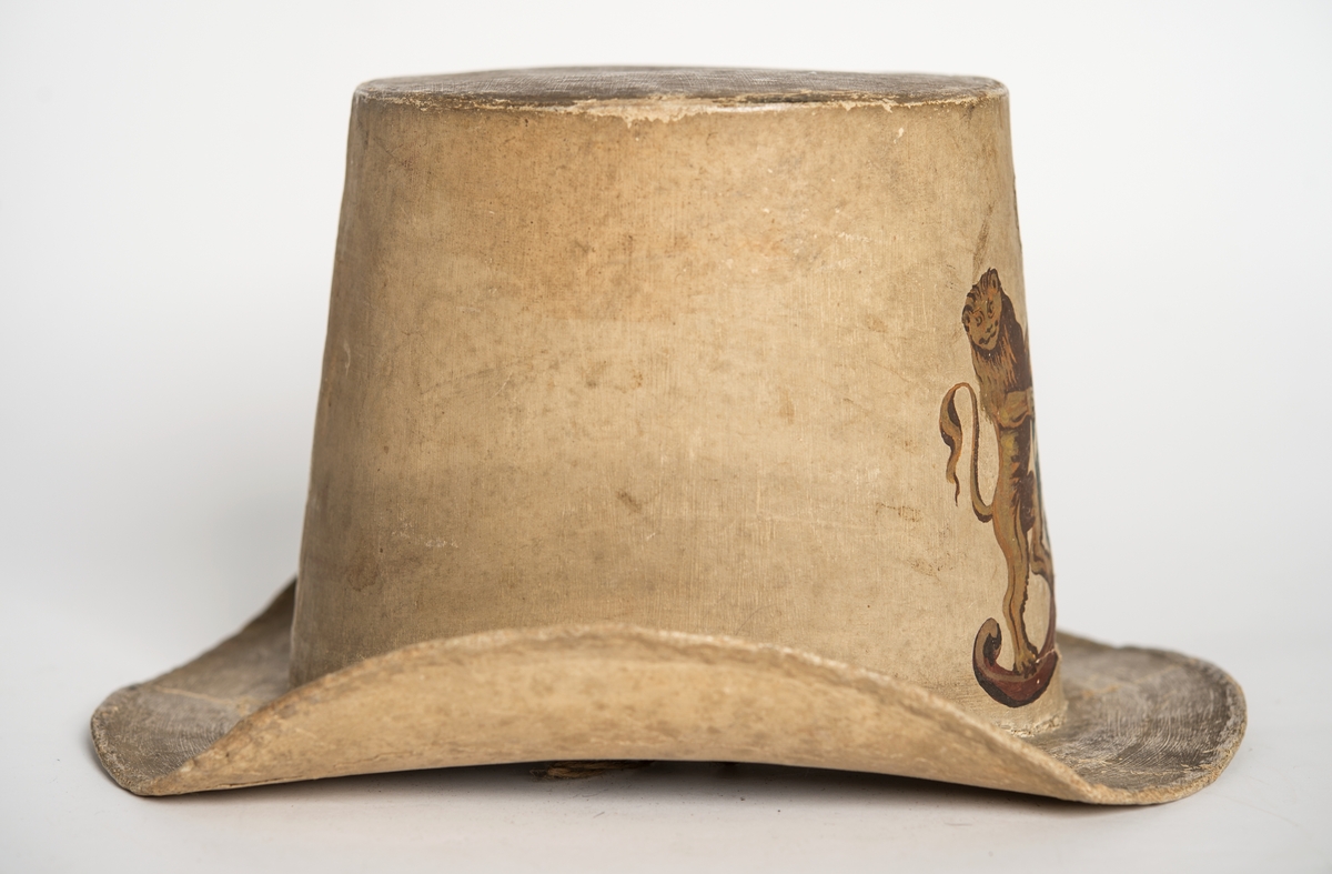 Hatt tillverkad av papp som målats med en crémegul färg. Framtill försedd med svensk-norska riksvapnet i färg. Foder av bomullstyg, 115 mm brett och dragsko.