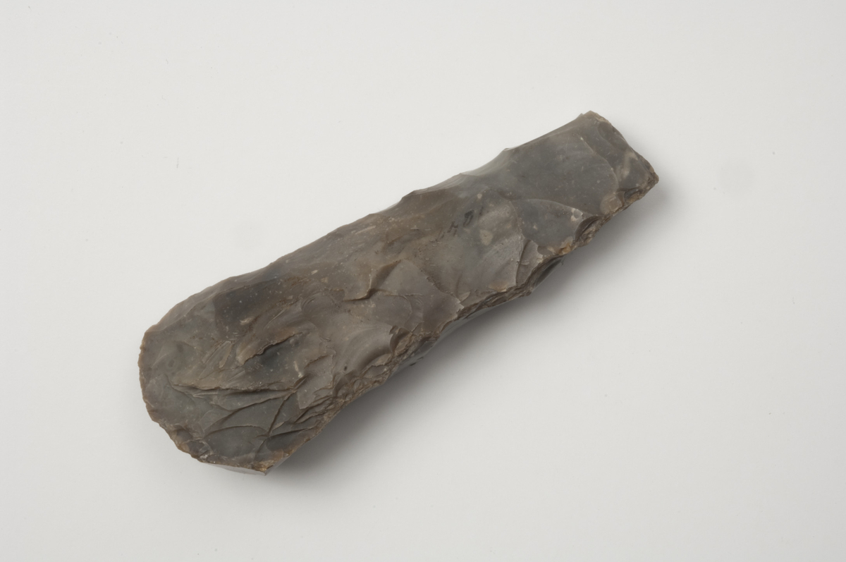 "1042-49. 8 Emner til Retmeisler af forskjellig Størrelse. Graa Flint. Længden varierer mellem 15 og 10 cm, Eggens Bredde mellem 6 og 3,5 cm. No. 1043 har udsvingede Eghjørner. De øvrige har afrundet Eg." Ny beskrivelse etter revisjon: 
Emne til øks av flint, stl: 158 mm, stbr: 58 mm.