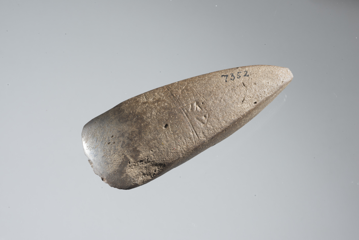 "Steinøks uten skafthull av Gotlandsk type, sl. Gutorm Gjessing: Norges steinalder s. 332 fig. 117. 10,9 cm lang, 4 cm bred. - På den ene bredside er innskåret tre runer: x F P." Ny beskrivelse etter revisjon: Firsidig øks av bergart med svakt hvelvede bredsider, rettstilt egg og spiss nakke. På den ene bredsiden er det innskåret tre runer, mens det på den andre er innskåret et slags strekmønster. Øksens stl: 109 mm, stbr: 40 mm. Ingvild Grønbecks kommentar til innskriften: De tre runene er, lest fra venstre mot høyre, hhv. en g-rune, en a-rune og enten en w-rune eller ev. en þ-rune (thurs), og hører til den eldre runerekka, som var i bruk fra 1.- 6./7. årh. e.Kr. Innskriften er rammet inn i underkant av flere innrissede, horisontale streker. I overkant er det en kortere strek som ikke strekker seg over hele innskriften. Det er også risset flere korte, mer eller mindre horisontale streker både mellom og tvers over noen av runetegnene - især mellom g-runen og a-runen.