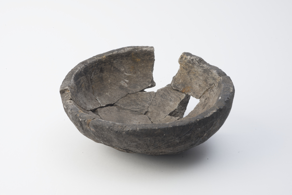 "7705 d. Lite lavt bolleformet kar av kleberstein av typen R. 729. Karet er 19,8 cm i tverrmål og bare 7 cm høyt." Ufullstendig, sammenlimt kleberkar i samsvar med beskrivelsen.