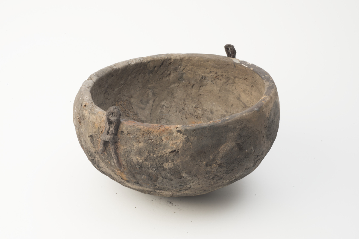 "2500 a. Klæberstensgryte, 25 cm i ydre tvermaal over kanten og 12 cm høi. Den er forsynet med jernhank og jernører."  
Bolleformet kar av kleberstein med største diameter over buken. Rand diam: 250 mm, største bukdiam: ca 270 mm. Karet har 'tobente' jernører som Redskaper fig. 191. Ene øret knekt og limt på igjen. Karet er sterkt sotet utvendig. Deler av karet er 'restaurert' med gips. Hanken av jern er bevart i tre, ikke sammenpassende fragmenter og ett stykke gips, omtrent halvparten av hanken mangler. Hankens br: 11-14 mm.  Fragmentenes stl: 128 mm (endestykket), 72 mm og 40 mm. Gipsrekonstruksjonen 68 mm lang.