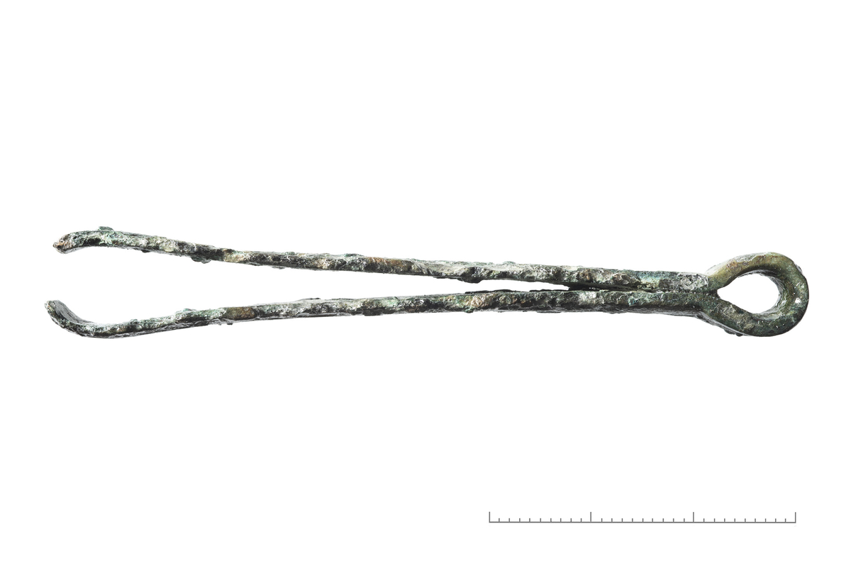 "2687 c. Pincet af bronce med ring i øiet, lignende R. 165, men noget bredere. Den er 7,3 cm lang." Ny beskrivelse etter revisjon: Pinsett av bronse med flate armer, dekorert med to grupper av smale furer. L.: 73 mm, br.: 7-9 mm. Bittet og ene langsiden på begge armer noe oppspist av korrosjon. Originalflaten mye skadet av korrosjon. Ringen mangler.