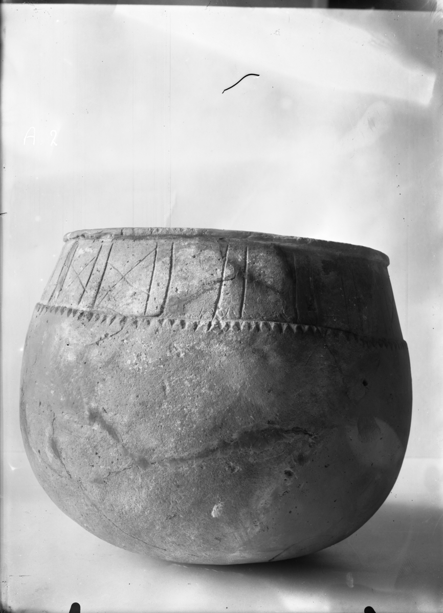 Urne af klæbersten, af form lig S. M. no. 2269 (S. M. aarh. 1900, fig. 8, pag. 76). Den er 19,5 cm høi, 19 cm vid over randen. Den indskaarne baard er inddelt i flere felter ved ophøiede vertikale ribber, der staar stillede parvis.