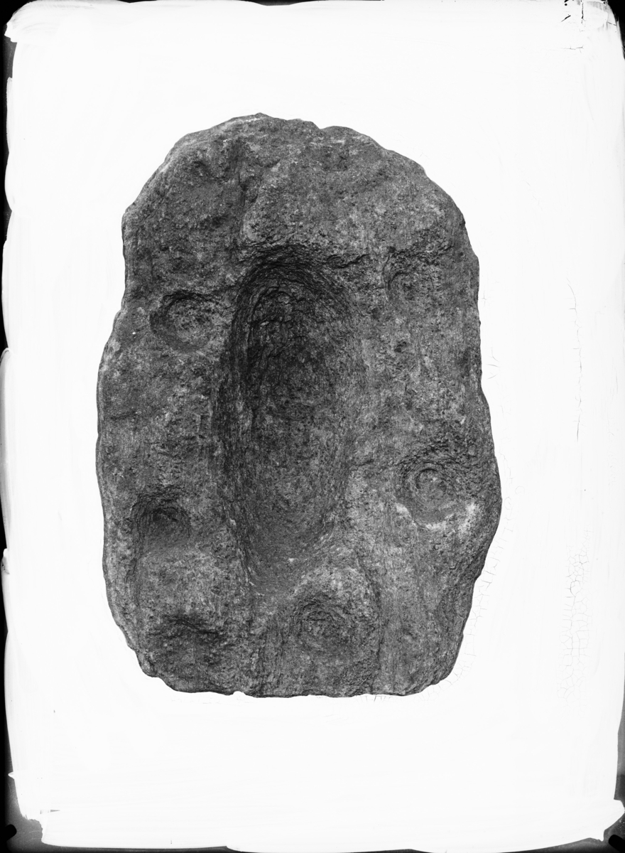 "Avlang helle med skålformede fordypninger, 46 cm. l., 32 cm. b. og ca. 4 cm. tykk. På midten er der en avlang, ganske dyp, forsenkning, 27 cm. l. og 11 cm. b. Omkring denne er gruppert 5 almindelige runde skålformede fordypninger med et tverrmål fra 4-6 cm. Der er plasert to huller ved hver av langsidene av den avlange grop og en for nedre ende av denne. På baksiden av hellen er også påbegynt en liten skålformet fordypning."  I samsvar med beskrivelsen.
