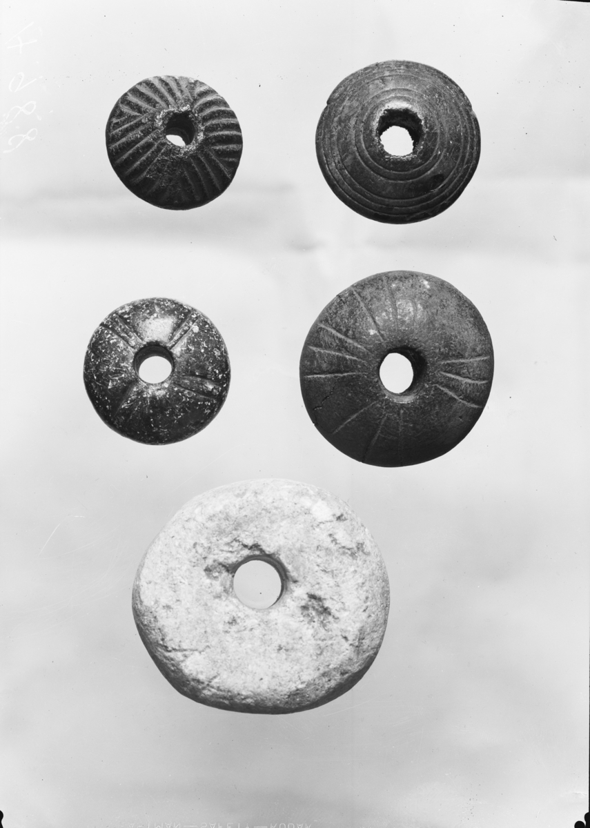"Vakkert spinnehjul av kleberstein fra folkevandringstiden av type som Gamle gårdsanlegg II Pl. XLI fig. i med samme ornamentikk av vertikale linjebunter. Tverrmål 3,4 cm., tykkelse 2 cm." Ny beskrivelse etter revisjon: Spinnehjul av grønn, polert kleber med hvelvet basis, hvelvet topp, var. II C. Dekorert på over- og underside med fire doble eller tredoble streker som sammen danner et litt skjevt kors rund hvert hull. H: 20 mm, t: 14 mm, diam: 35 mm, vekt: 35,4 g.