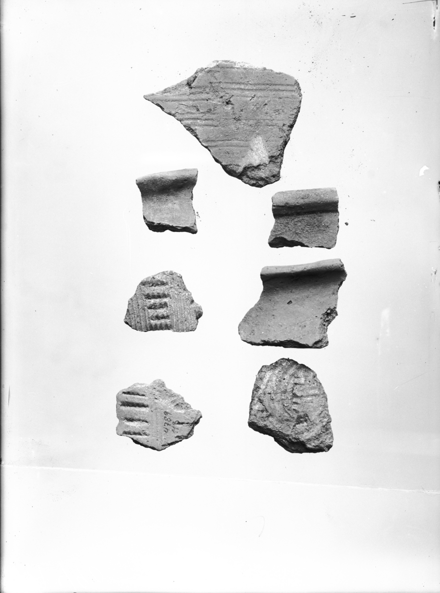 "4789 a. 153 lerkarstykker de fleste ganske små. Blandt disse stykker er en hel del (43) av de spannformede lerkar, deriblandt to som Ab. 1904 s. 55 fig. 22 med rekker av fire-fem eller seks-tannete innstemplinger mellem flere horisontale linjer, to andre stykker har flere buede paralelle linjer, andre har vertikale eller horisontale linjeborder. Bare få av de andre lerkarstykker har ornamenter, derav ett med et bånd som en efterligning av en snor, et annet med små hakk langs overkanten, et tredje av tynnt rødlig gods med strekornamenter som R. 361, et fjerde har rekke av tresidige små hakk mellem horisontale linjer; endelig er et stykke en del av en hank. De fleste er imidlertid av grovere tykkere gode uten ornamenter. Av overkantstykker kan det sees at der minst må ha vært 3-4 av slike lerkar. Et par overkantstykker viser sterkt utbrettet profil (avb. Gamle gårdsanlegg 1933, pl. 1, fig. 1-2)."
Hundreogfemtito skår av leirkar hvorav femtitre av dem er av spannformede og nittini av andre leirkar. Skårene av de spannformede leirkarene har fått egen underbokstav (k). Blant de andre skårene er det minst ni ulike leirkar hvorav tolv randskår og ett bunnskår. To av skårene er fra overgang mellom vegg og bunn, og to er fra hanker som har tilhørt karene. Seks skår har dekor. Skårene er mellom 12 og 52 mm (st) L. (1) Karet består av minst sju skår. Randen er utoverbøyd, fortynnet og spiss. Det ene hankeskåret hører sannsynligvis til her. Skårene er ca 8 mm tykke. (2) Karet består av minst ett randskår. Randen er kraftig utoverbøyd og avrundet. Skåret er 7 mm tykt. (3) Karet består sannsynligvis av minst fjorten skår. Randen er utoverbøyd, fortykket og avflatet. Skårene er 6 - 8 mm tykke. (4) Karet består av minst sju skår. Randen er utoverbøyd. To av de dekorerte skårene hører sannsynligvis til her. Det ene er dekorert med tresidige hakk og det andre med strekornamenter, som beskrevet ovenfor. Skårene er 3 - 6 mm tykke. Noen av dem er sekundært brent. (5) Karet består sannsynligvis av minst tjueto skår. Skårene er 5 - 8 mm tykke. Randen er avflatet og har en innvendig lippe. To av de dekorerte skårene hører sannsynligvis med her. Det ene er dekorert med et snorlignende bånd, som beskrevet ovenfor. Det andre har bare en rett kant. (6) Karet består av minst ni skår. Randen er svakt utoverbøyd og avrundet. 6 - 7 mm i tykkelse. (7) Karet består sannsynligvis av seks skår. Randen er fortykket og avrundet. Avskrådd innvendig. Et hankeskår hører sannsynligvis med til dette karet. Skårene er mellom 8 og 11 mm tykke. (8) Karet består av minst ett skår. Randen er rett og avflatet med utvendig lippe. Karveggen svinger utover 20 mm under randen. Skåret er 5 mm tykt. (9) Karet består av minst to skår. Randen er utoversvunget med utvendig lippe og er dekorert med små hakk, som beskrevet ovenfor. 6 mm i tykkelse.
