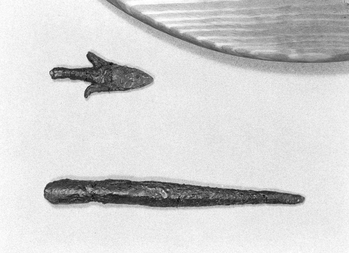 "Kastespydspids af jern, lignende Rygh 202. Den er 11,3 cm lang, hvoraf falen er 4,2 cm. Kun paa den ene side er udhugget en agnor i lighed med Rygh 210." 
Ny beskrivelse etter magasinrevisjon i 1999: Liten spydspiss med to mothaker, stl: 92 mm, bladets l (inkl. mothaker) 60 mm. Skafthalsen er meget spinkel og knekt, stl: 39 mm, diam. ved bruddet: 9-10 mm. Spissen er kraftig, og galt  'restaurert' med gips. Røntgen  viser at mesteparten av bladet består av gips, med noe jern i odden. Den ene mothaken er del av en ring, nagle el. lign. og har ingen sammenheng med den originale spissen, som består av skafthals, bladrot og en mothake. Avbildet i VJG fig. 117.