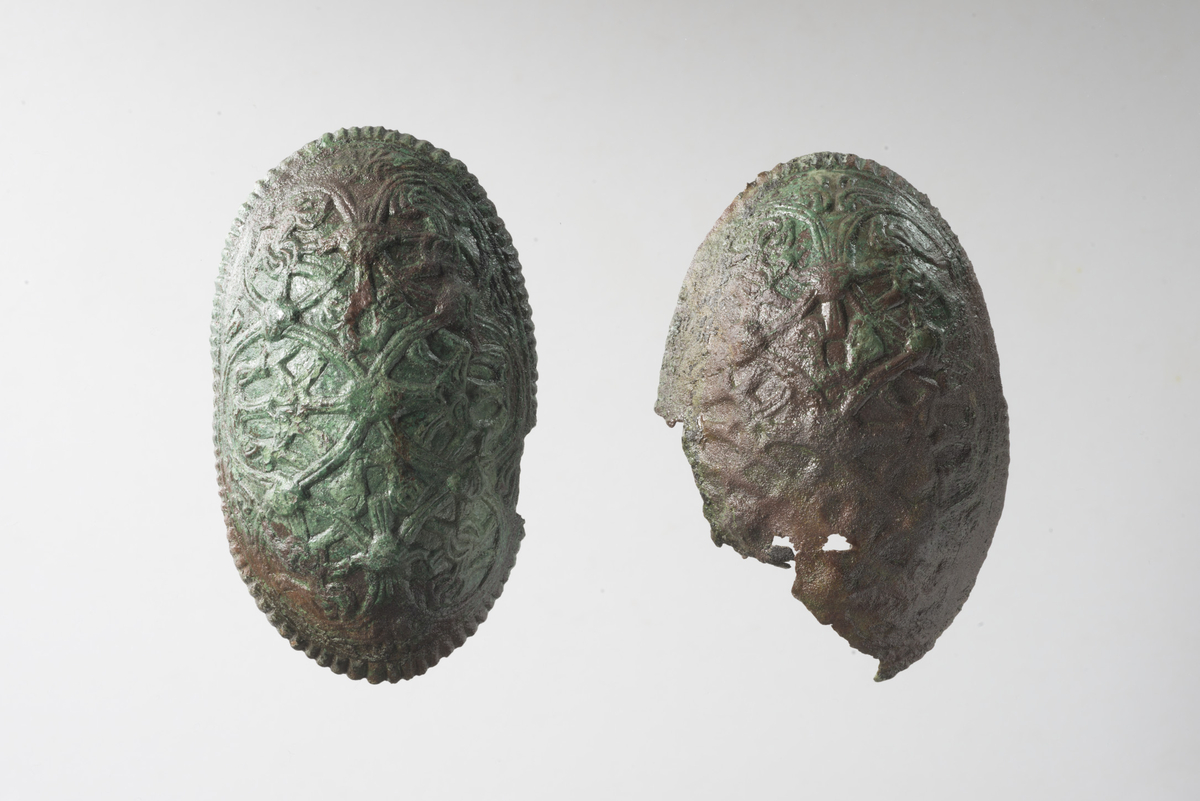 10969. To  skålforma spenner av bronse, som  Petersens 1928: fig. 46 side 52. Den ene spennen er nesten hel, bortsett fra et ca. 20 mm stort stykke som mangler, fra midt på brosjen mot enden. Kanten på andre langside er litt skadet. St.l 116 mm, st. b. 62 mm, st. h/t 27 mm. På baksiden er rester av nålen korrodert til nålefestet. Kroken for å feste nålen er intakt.
Den andre spennen er mer skadet. Ca. 70 mm av kanten er borte fra midt på langsiden til midt på kortsiden.  Det er ikke rester av nålen igjen, bare festet. Kroken for å feste nålen er intakt. St. l. 112 mm, st. b. 66 mm, st. h/t. 27mm.