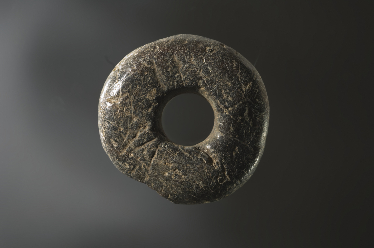Spinnehjul av kleber med rett basis og toppflate. Sideflatene er lett konvekse med kraftigere krumming ved basis og toppflaten. Sidekantene i tenhullet er parallelle. Spinnehjulet har en god del riper i overflaten, og en del av sideflaten er skadet. Std.: 35 mm, stt.: 11 mm. Std. tenhull: 11 mm.