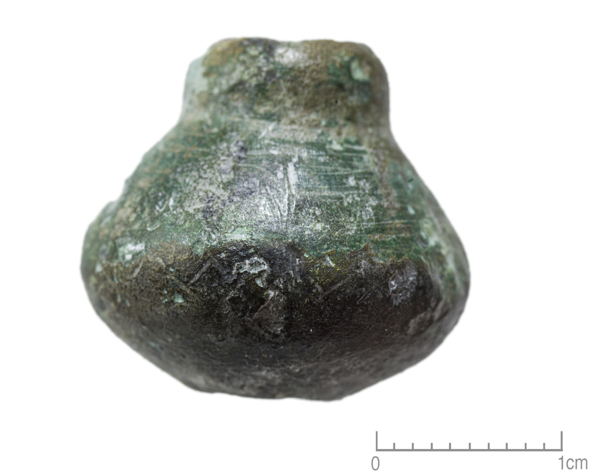"Spinnehjul av bronse, dobbelkonisk med en høyt oppstikkende krave rundt hullet på oversiden, sl. R171. Diameter 2,1 cm." Ny beskrivelse etter revisjon: Spinnehjul av bronse med rett basis- og toppflate og konvekse sideflater. Sylindrisk overdel rundt den øvre tenhullåpningen som R171. Dekorert med en 2 mm br. sikk-sakk bord på st.diam, delvis bevart to smale rundtløpende riller på toppflaten nær den sylindriske overdelen. Diam: 22 mm, sth: 20 mm, vekt: 29,6 g.