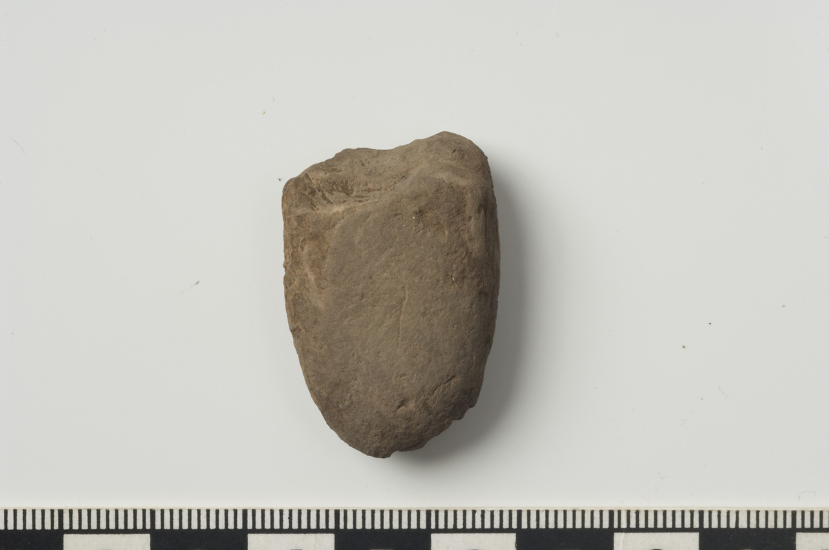 En firsidig øks/meisel av bergart. Gjenstanden har slipte flatsider og enkelte avspaltninger i eggen. L:33 mm, Br:23 mm, T:11 mm. (Fnr. 57).
