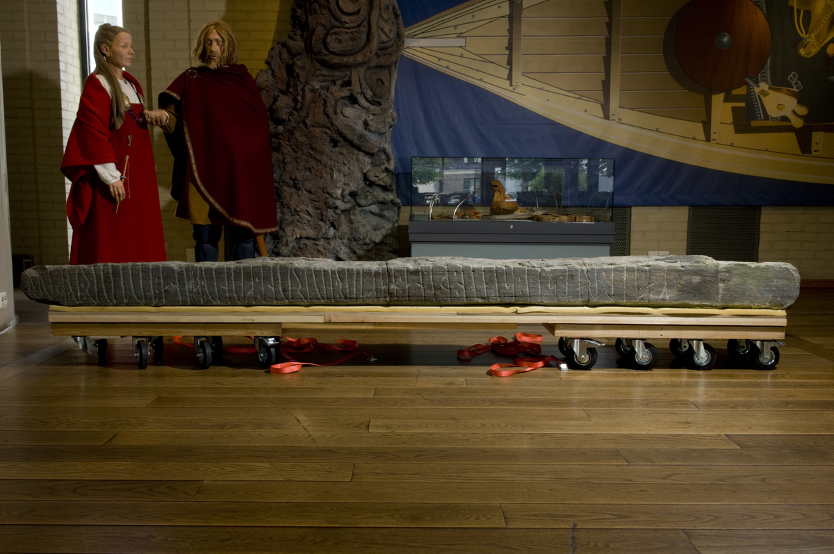 Runestein (Mariakirken) med en linje med runer på én side. Steinen består at fire sammensatte deler, h: 3,49 m, stbr: 23 cm, stt: 27 cm. Når steinen var reist har den raget 3,12 m over bakken, skillet er meget tydelig på steinen. M. Olsen har tolket innskriften slik: "Ketil reiste denne sten efter Jorunn, sin kone, datter av Utyrme (?)"