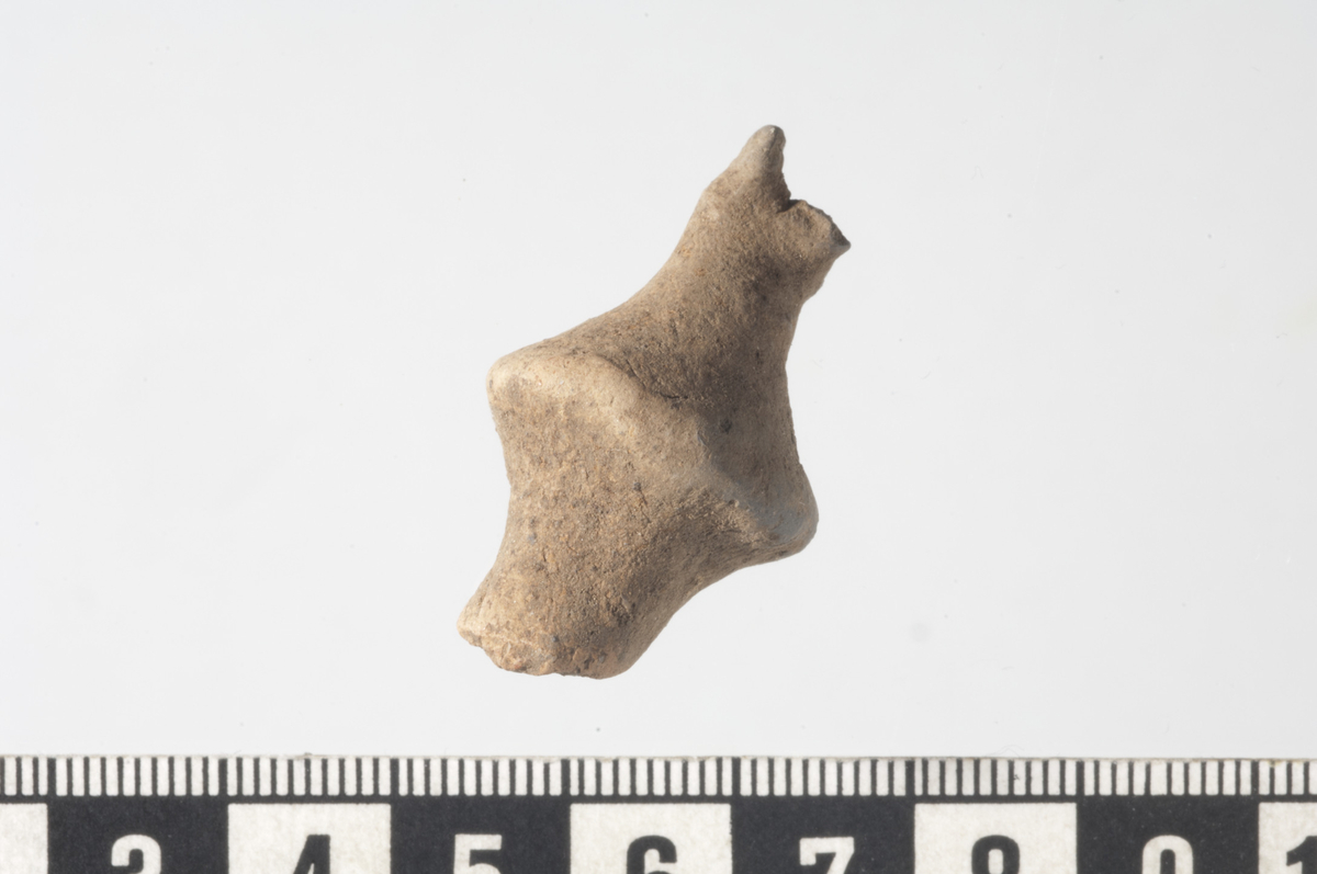 3,5 cm lang propplignende gjenstand i brent leire.Gjenstanden har en dobbelkonisk form med et markert "hjul" i midten. Fra midten går det ut to stenger. Den ene siden er brukket, den andre siden er 1 cm lang og avsluttes i form av fire små tapper, som en kroneform. Det er foreslått at gjenstanden har vært en form for propp/stopper og at den har forbindelse med metallhåndverk.
