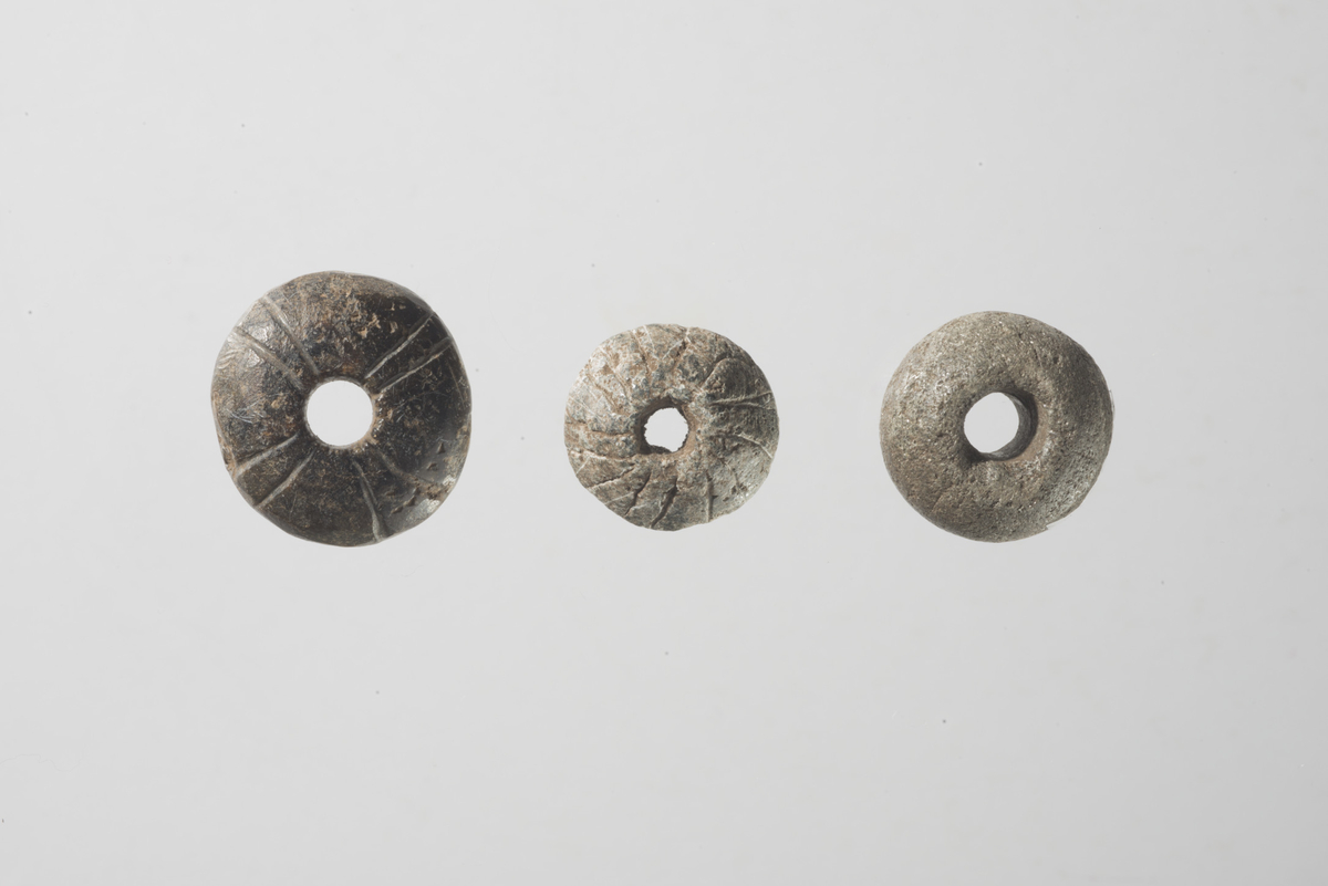 Spinnehjul av kleber med rett basis og hvelvet topp. Dekorert med et kors/solsymbol. Slitt og polert på undersiden. Små hakk etter tråd ved tenhullet, som har en diameter på ca. 0,9 cm.  