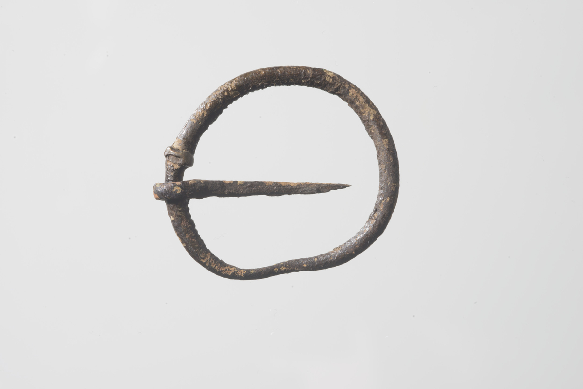 Ringspenne av kobberlegering lik type 2.1. (Søvsø 2009) med bevart nål. Rammen har rundt tverrsnitt men varierende tykkelse trolig på grunn av korrosjon. Spennerammen har diam. 26 mm og indre diam. 21 mm. Rammen er delvis korrodert og skjev. Nålen når ikke tvers over hele rammen og er trolig knekt/korrodert i spissen. Nålefestet har form av en rundtløpende vulst på rammen. Det kan være spor av riflet overflate på rammen.