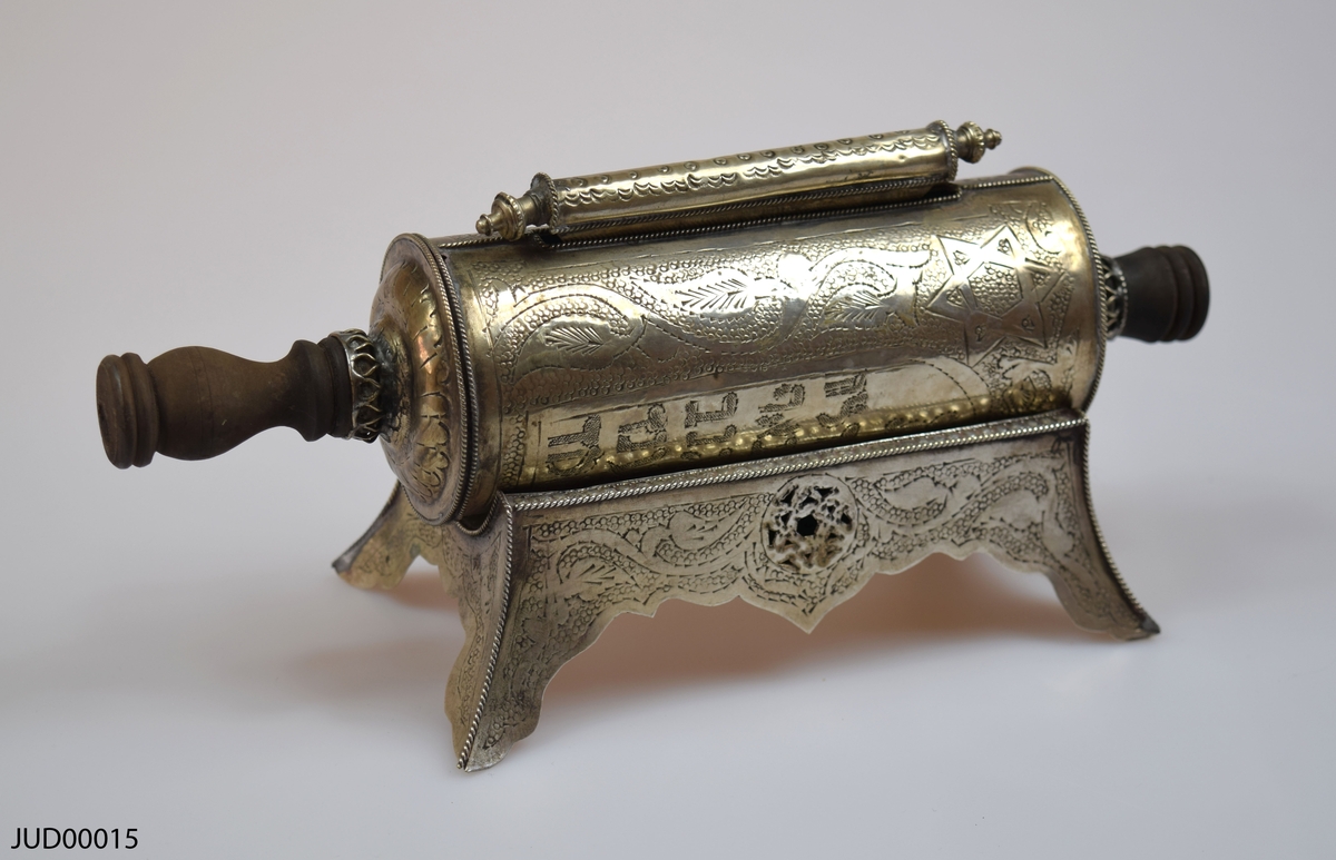 En tom silverrulle med trähandtag för Megillat Ester, med tilllhörande  stöd för rulle samt fäste för texten som båda är tillverkade av silver. Rikt dekorerad i form av gravyr, föreställande bland annat de tio budorden på hebreiska.