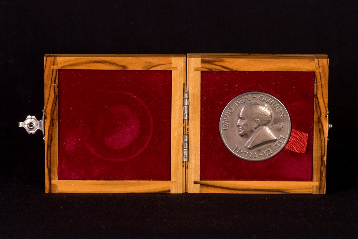 Bronsmedalj med tillhörande träetui, klätt invändigt med röd sammet. Lås på etuiets framsida, tillverkad av metall. Medaljen är dekorerad med text på fram- och baksidan, samt en läsande arbetare på ena sidan och en man i profil (David Den Gurion) på andra sidan.