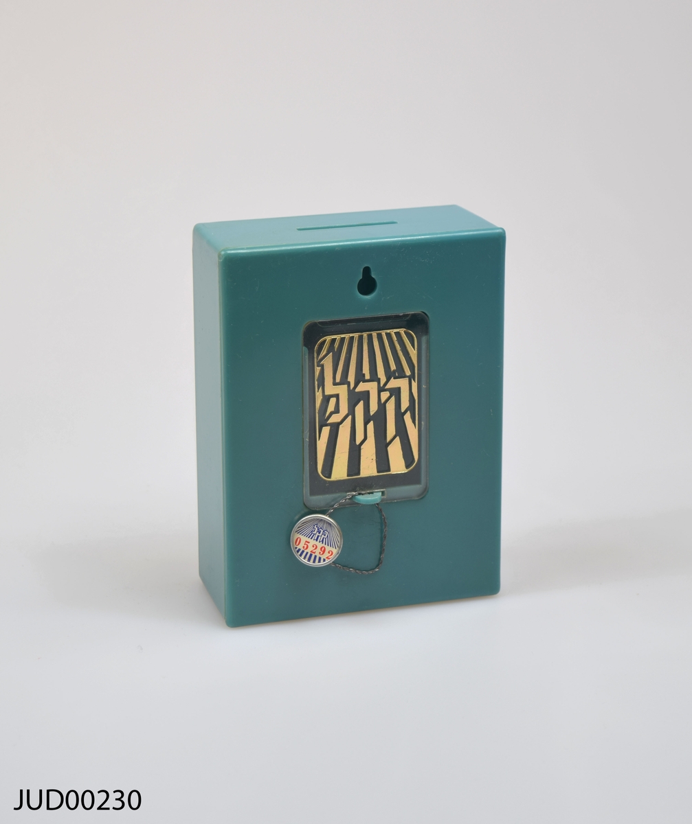 Grönblå insamlingsbössa med vit dekor. Dekorerad med stjärna, karta samt hebreisk text. Knapp fäst på bössan, på vilken det är skrivet med hebreisk text samt nr 05292.