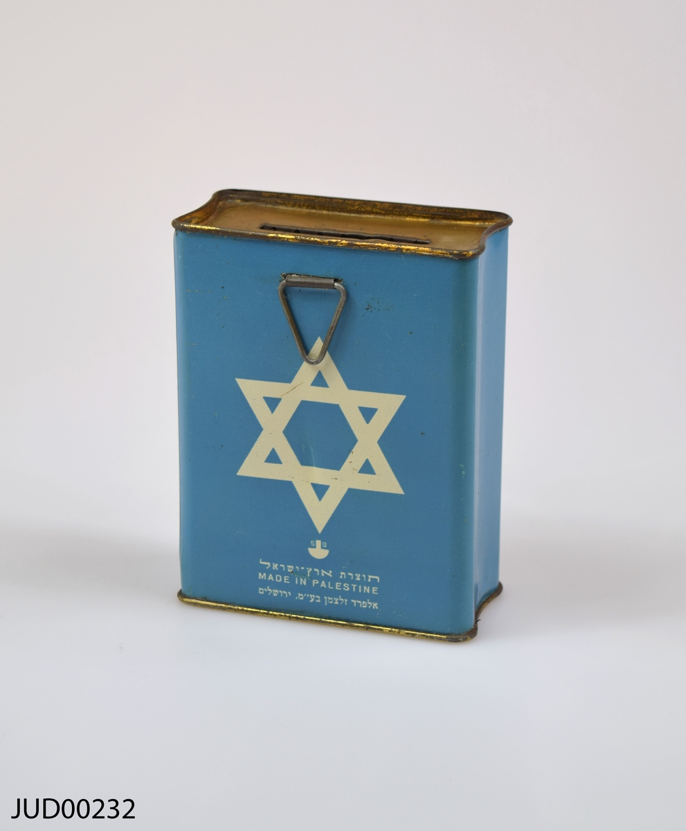 Insamlingsbössa, tillverkad av plåt och sedan målad med blågrön färg. Dekorerad med vit stjärna samt hebreisk text. Låst och saknar nyckel.