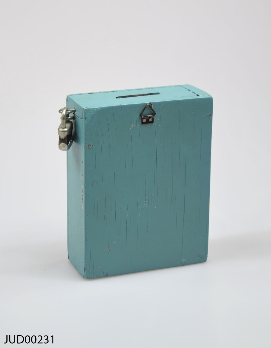 Insamlingsbössa, tillverkad av trä och sedan målad med turkos färg. Hänglås fastsatt på ena sidan.