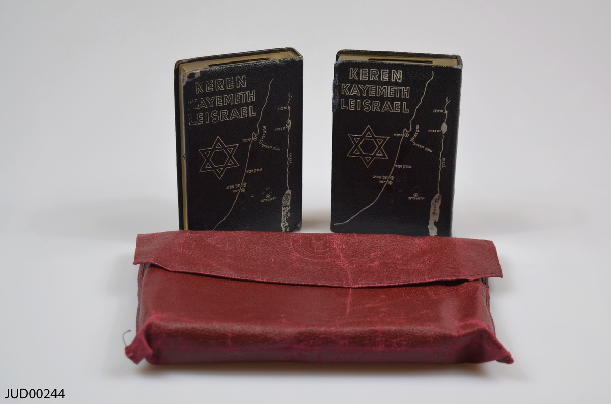 Två stycken insamlingsbössor utformade som böcker, tillverkade av mässing. Silvrig dekor i form av Davidsstjärna, karta över Israel samt hebreisk text. Även dekorerad med följande text:
Keren Kayemeth Leisrael
JNF Jerusalem