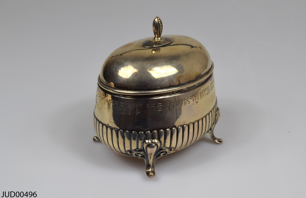 Silverask, med lock fastsatt på gångjärn. Står på fyra korta ben. Enkelt dekorerad med ristad hebreisk text.