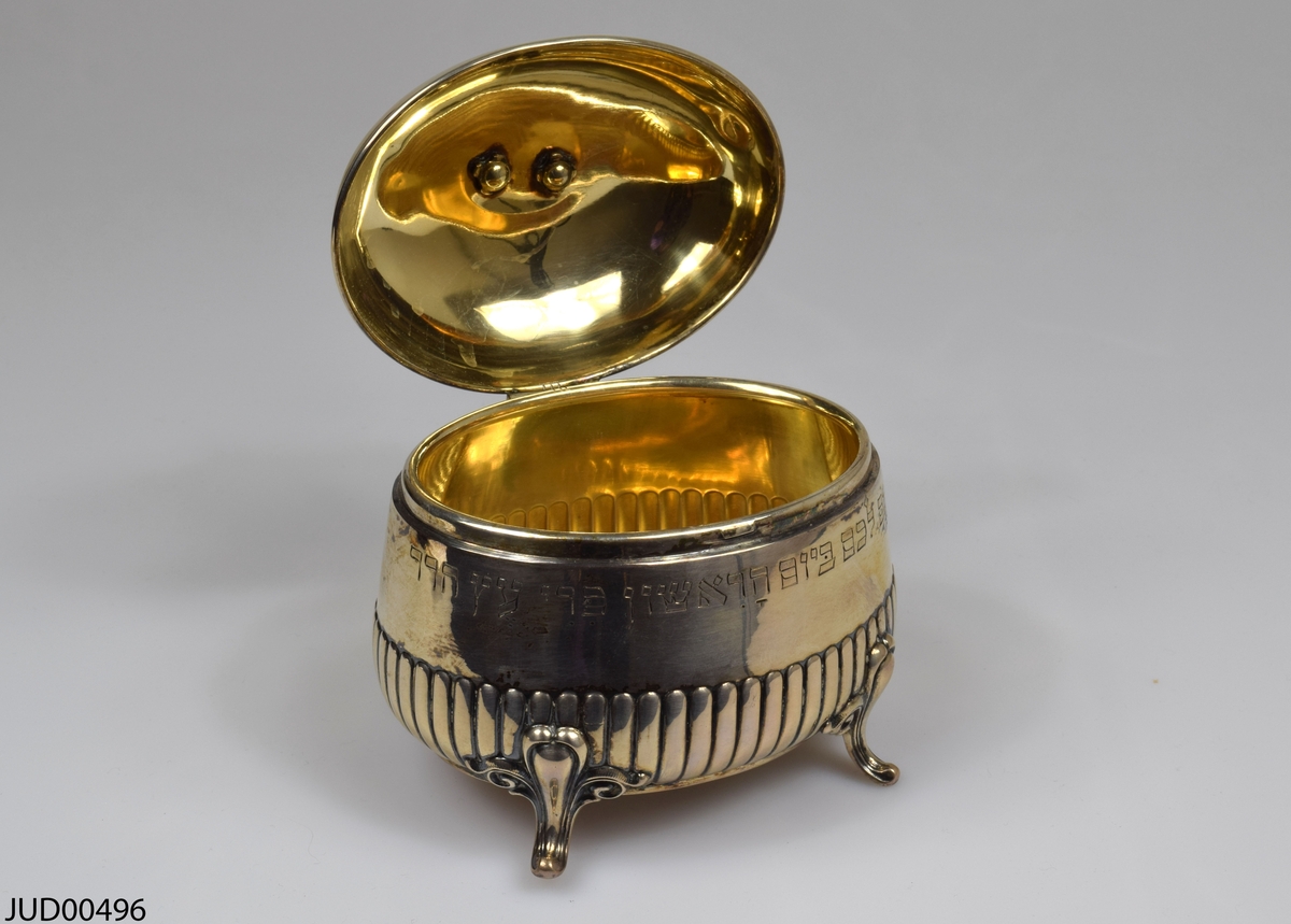 Silverask, med lock fastsatt på gångjärn. Står på fyra korta ben. Enkelt dekorerad med ristad hebreisk text.