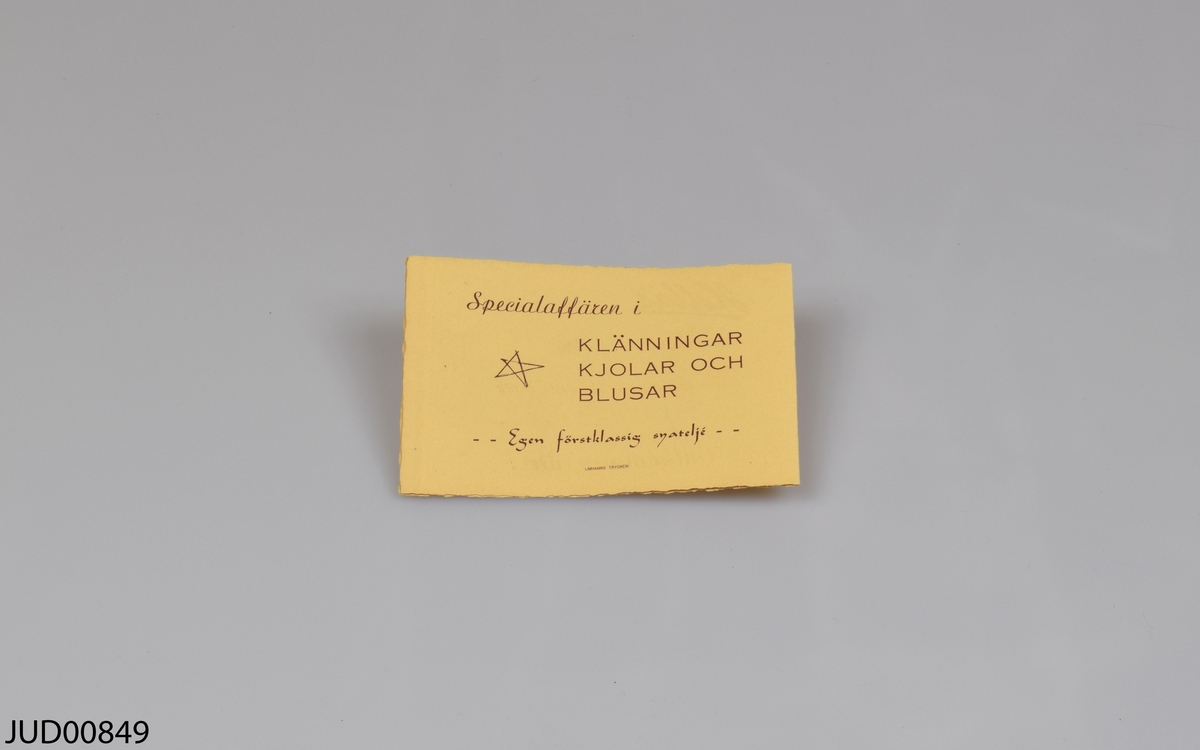 Galge, tillverkad av trä med en krok av metall. Tryckt svart text på fram- och baksidan.