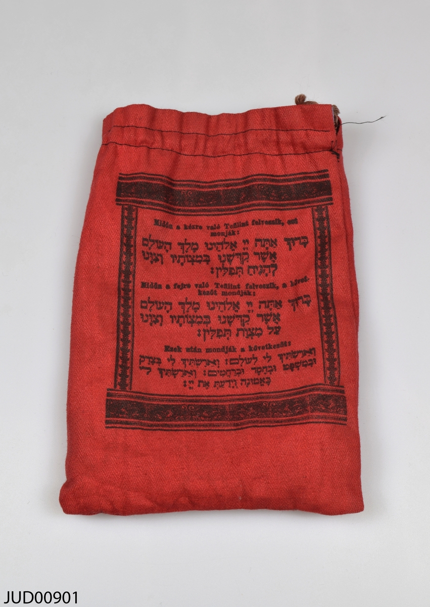 Ett par tefillin (böneremmar) med tillhörande påse. Kapslarna är tillverkade av trä, medan remmarna är tillverkade av svart läder. Påsen är tillverkad av rött tyg, och påsens insida är klädd med lilafärgat brokad. Påsen är dekorerad med svart hebreisk och ungersk text tryckt på ena sidan, medan påsens andra sida är dekorerad med stentavlorna tryckta i svart.