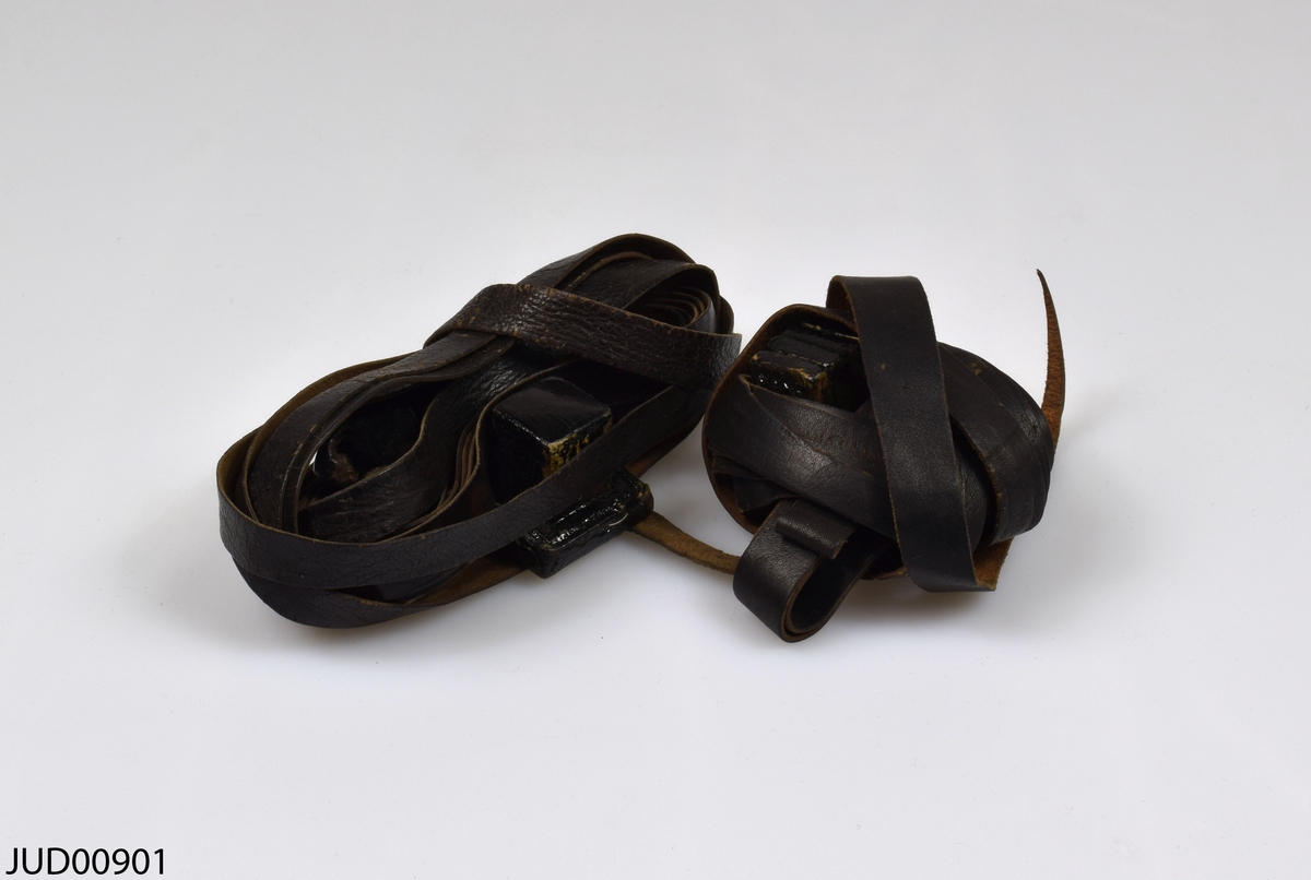 Ett par tefillin (böneremmar) med tillhörande påse. Kapslarna är tillverkade av trä, medan remmarna är tillverkade av svart läder. Påsen är tillverkad av rött tyg, och påsens insida är klädd med lilafärgat brokad. Påsen är dekorerad med svart hebreisk och ungersk text tryckt på ena sidan, medan påsens andra sida är dekorerad med stentavlorna tryckta i svart.