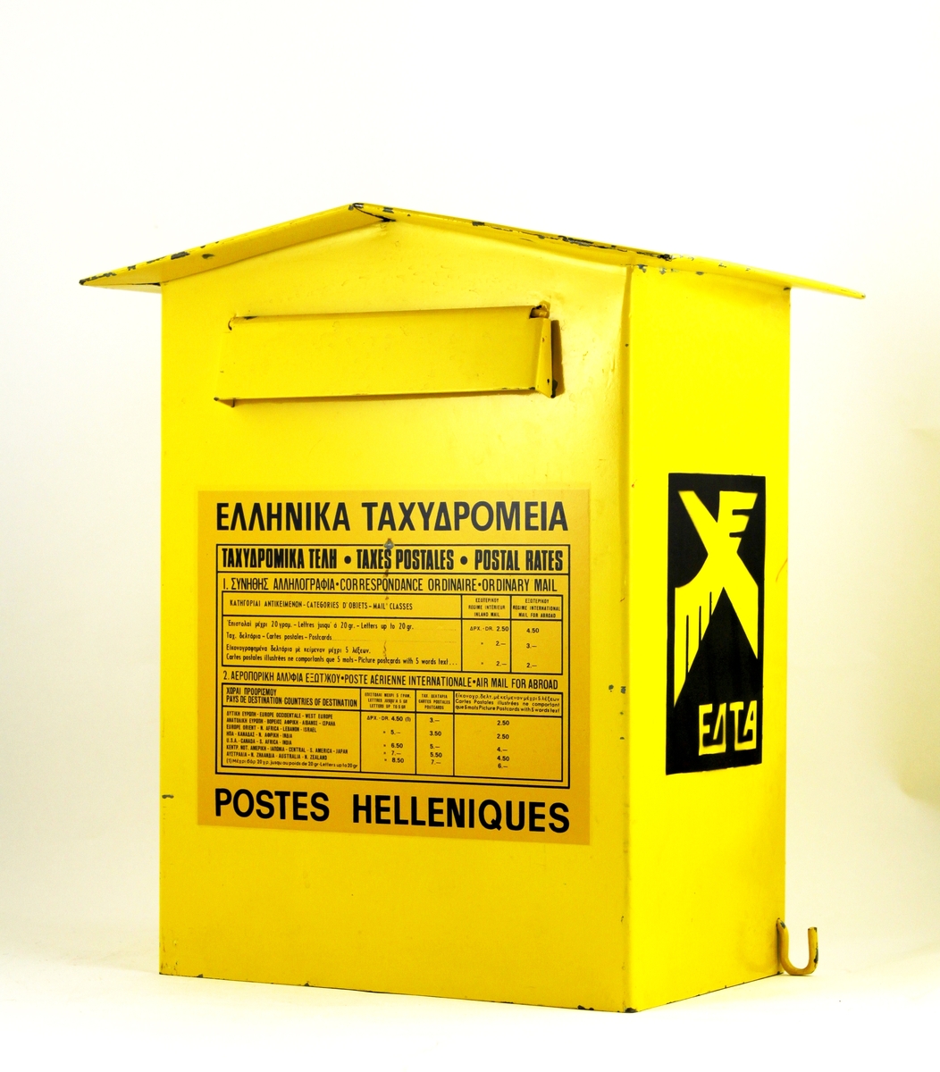 Brevlåda från Grekland. 

Spetsigt tak. Brevinkast på framsidan. Töms genom lucka i lådans botten. Det sitter krokar på lådans sidor för upphängning av postväskan vid tömning. Postemblem på kortsidorna. På framsidan är en portotabell uppklistrad. Nyckel finns.