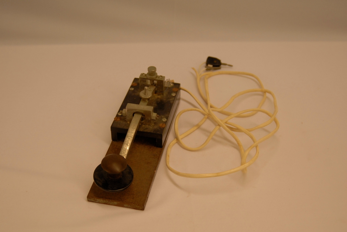 Rektangulær plate som det er festa ei stong med eit kulehåndtak på. Ein ledning med ein komponent på enden er festa til gjenstanden.