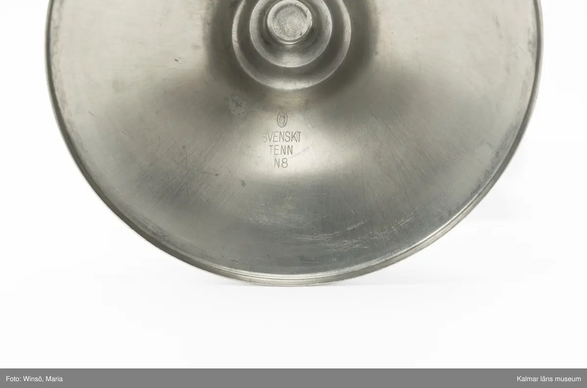 KLM 46137:3:1-2. Pokal, prispokal, lockpokal, metall, trä, färg. Prispokal i rokokostil med skål och fot i tenn (:3:1). Lock med dekor i form av bladrankor på toppen (:3:2). Skålen och foten binds samman av genombruten dekor i form av bladrankor. Foten är fastskruvad på svartmålad svarvad sockel av trä. Inskrift: POSTENS HEDERSPRIS "KVARNHOLMEN RUNT" 1941. Stämpel (insida lock): ortsstämpel för Stockholm SVENSKT TENN  N8.