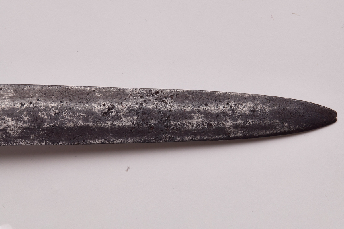 Tveegget sverd med flat klinge og brede egger. Parerplate, bøyle og knapp av jern. Kavle av tre med messingholker rundt endene. På klingen speilmonogram F 4 med krone over. På knappen H N0 5. solid parerplate som går over i en 3 cm lang stang med nedbøyd ende. Bøylen er en fortsettelse av platen og er svakt rundet og stukket inn i knappen. Eggformet knapp med spissen ned, knott på toppen der tangen er klinket. Kavlen har hatt surring av tvunnet messingtråd, rester av tråd sitter igjen under messingholkene. Klingens egg har huggsår.