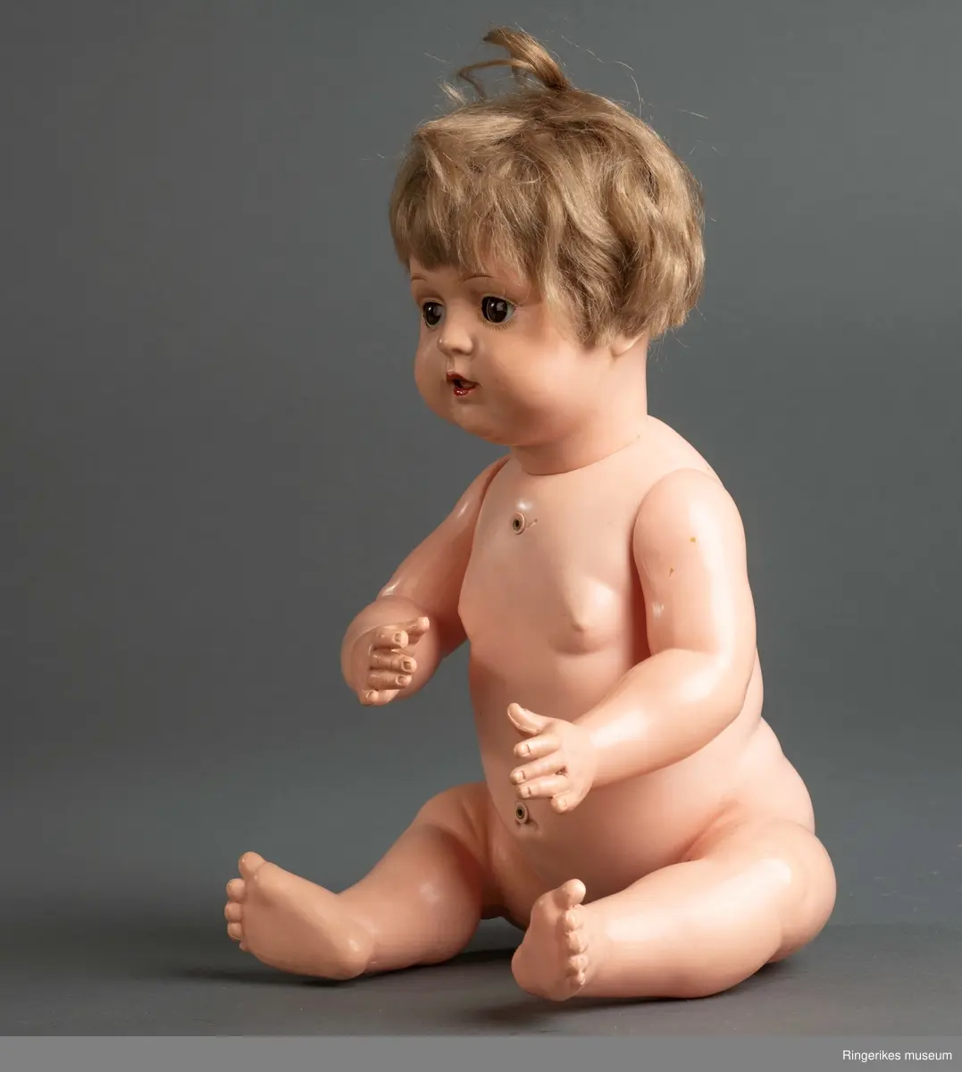 Stor dukke, litt babyfasong, bøyde arrmer og ben, øyne som kan som kan åpnes/lukkes og tykt hår. I kroppen lagt inn en boks som gir fra seg lyd ved bevegelse.