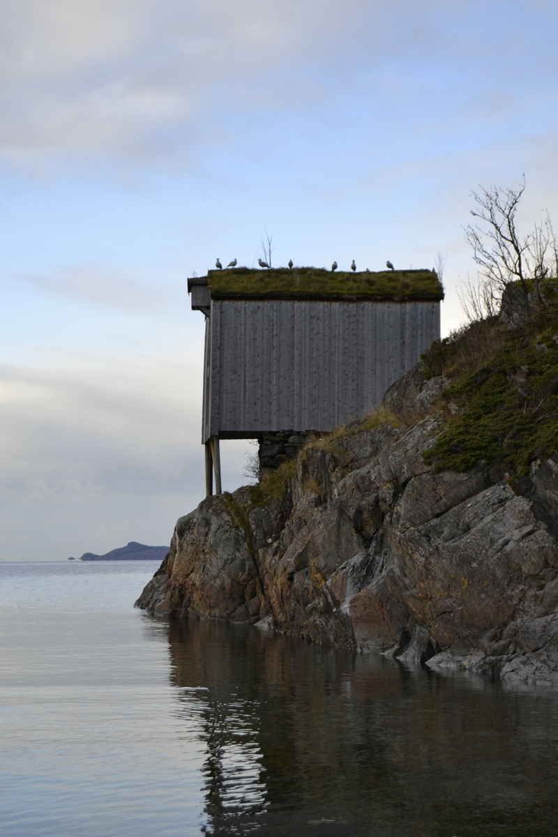 Brygge i to etasjer, stavkonstruksjon i første etasje med laftet overetasje. Tak tekket med plast og torv. Original kledning, dør og vindu. Vestveggen er skiftet. 