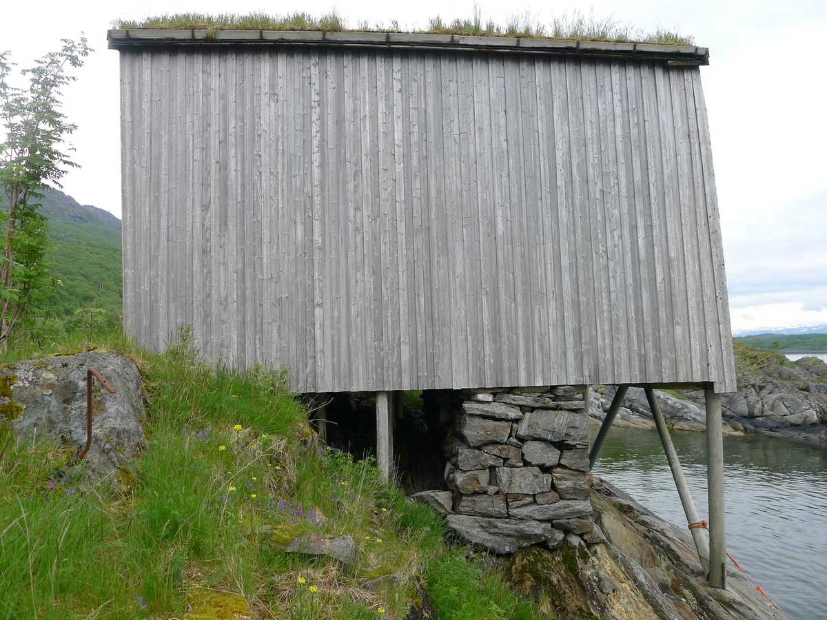 Brygge i to etasjer, stavkonstruksjon i første etasje med laftet overetasje. Tak tekket med plast og torv. Original kledning, dør og vindu. Vestveggen er skiftet. 