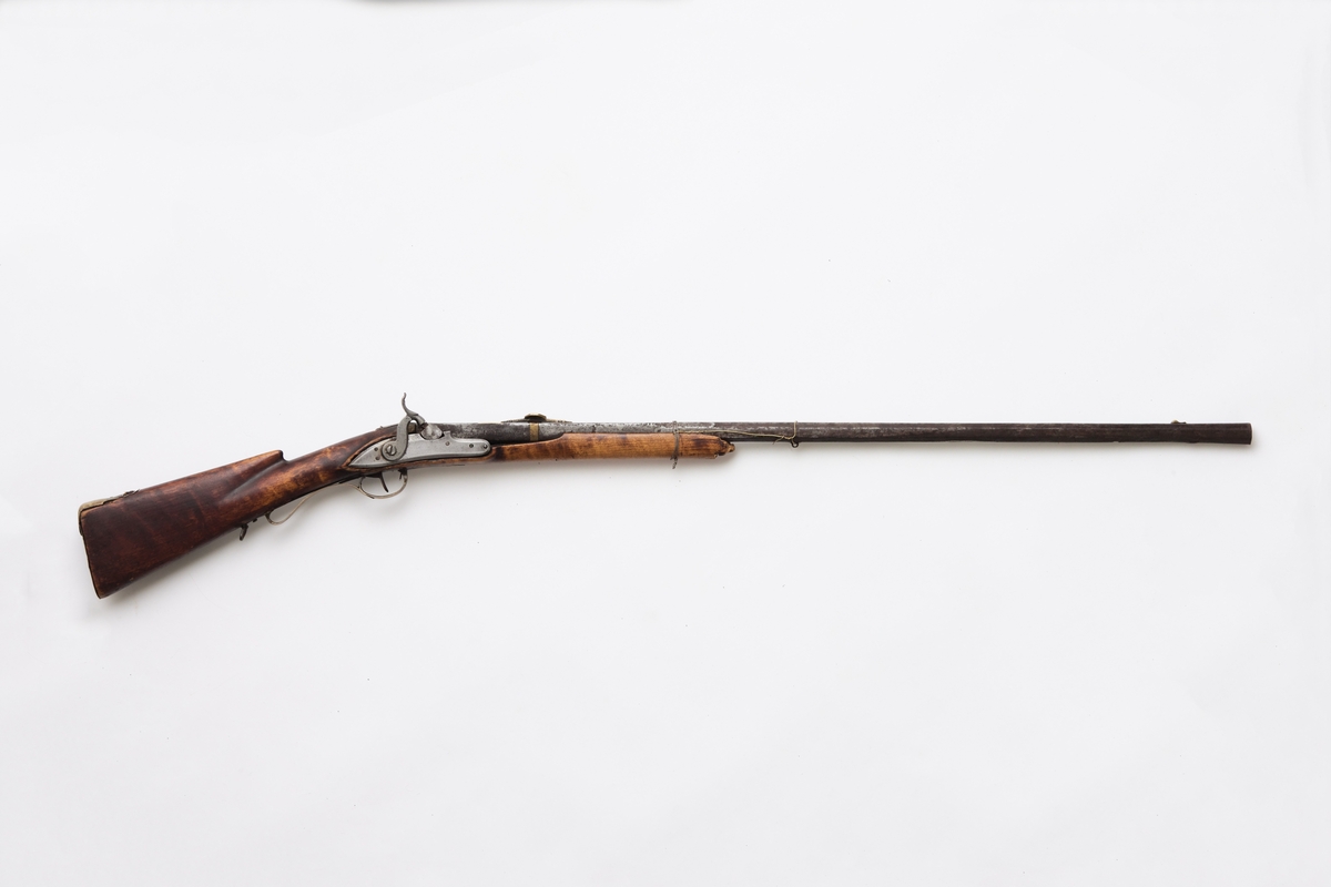 Glattløpet gevær med kassepipe og perkusjonslås. Skjeftet av bjørk, forskjeftet avbrukket 67 cm fra munningen, kolbekappe av messing, kolben har kinntre, bøyle og bøylebeslag av messing, geværet har hatt to stoppskiver istedenfor sideblikk, ved bakre låsskrue er endel treverk borte og erstattet med en tykk aluminiumsskive, forsikringer på hanen, pipens kammerende er firkantet, oppå er her prikket inn O T samt gravert I B ? S  ,langs begge kanter en fure, der pipen blir åttekantet er innslått enkel dekor, sikte av messing med V-formet skur og mange profiler festet med messingbånd rundt pipen.

Pipen er svampet, dvs at den er tykkest ved munningen.
Tydelig smedmerker på pipa.