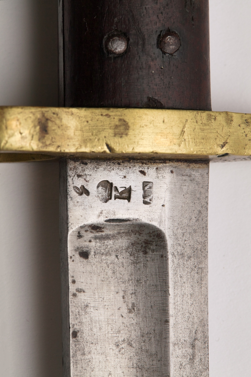 Sabelbajonett med jatangformet klinge, hulslipt, med tveegget spiss. Parerstang av messing, skjeftet av tre med en øvre del av messing. Parerstangens bakre arm danner en ring med diameter 23mm. Skjeftets øvre messingdel har spor for pipens bajonettklakk, låsingen skjer ved fjær og knapp av stål.