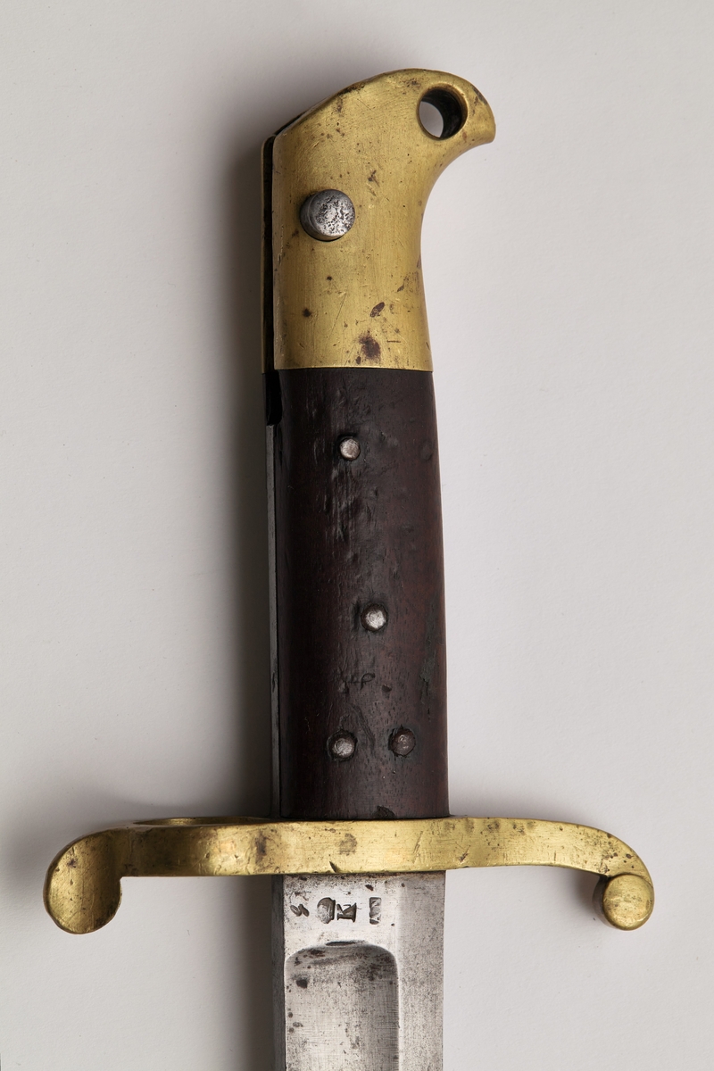 Sabelbajonett med jatangformet klinge, hulslipt, med tveegget spiss. Parerstang av messing, skjeftet av tre med en øvre del av messing. Parerstangens bakre arm danner en ring med diameter 23mm. Skjeftets øvre messingdel har spor for pipens bajonettklakk, låsingen skjer ved fjær og knapp av stål.