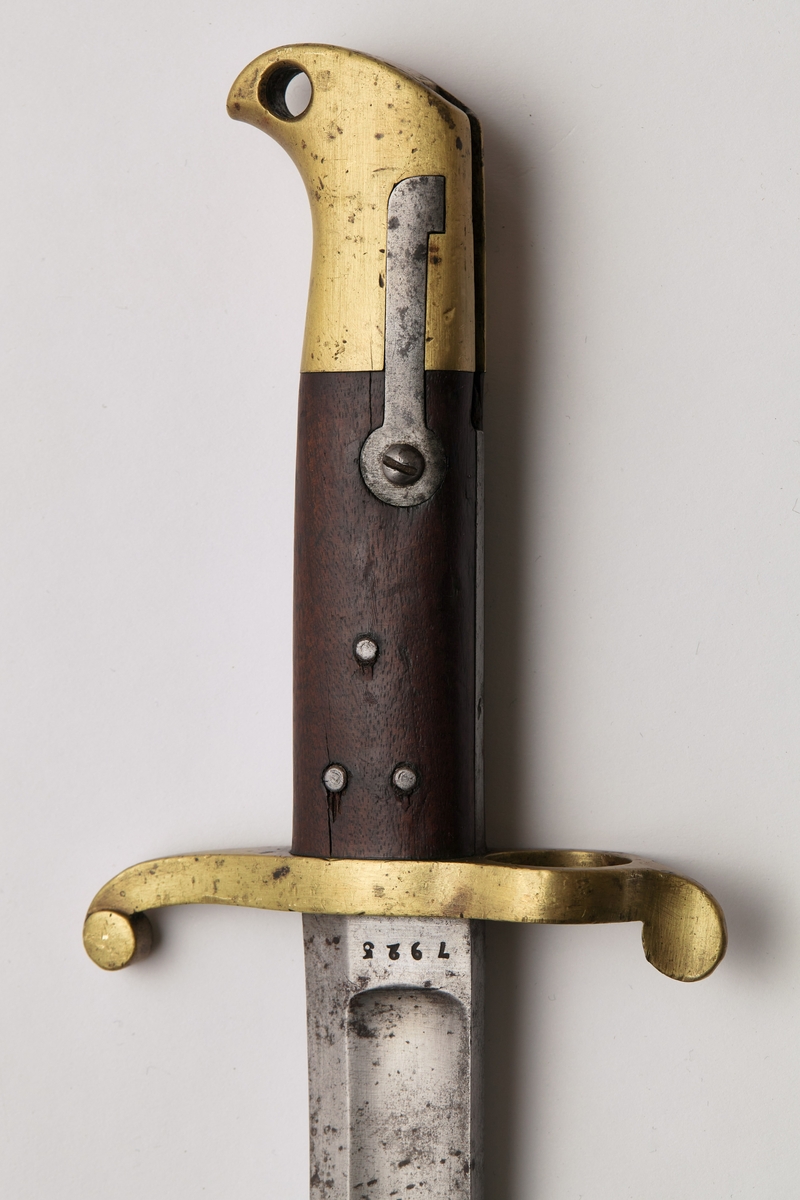Sabelbajonett med jatangformet klinge, hulslipt, med tveegget spiss. Parerstang av messing, skjeftet av tre med en øvre del av messing. Parerstangens bakre arm danner en ring med diameter 23mm. Skjeftets øvre messingdel har spor for pipens bajonettklakk, låsingen skjer ved fjær og knapp av stål.
