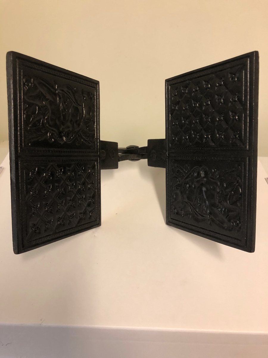 Langskaftet gorojern til bruk over åpen varme. Den ene siden er preget med Adam og Eva som motiv.