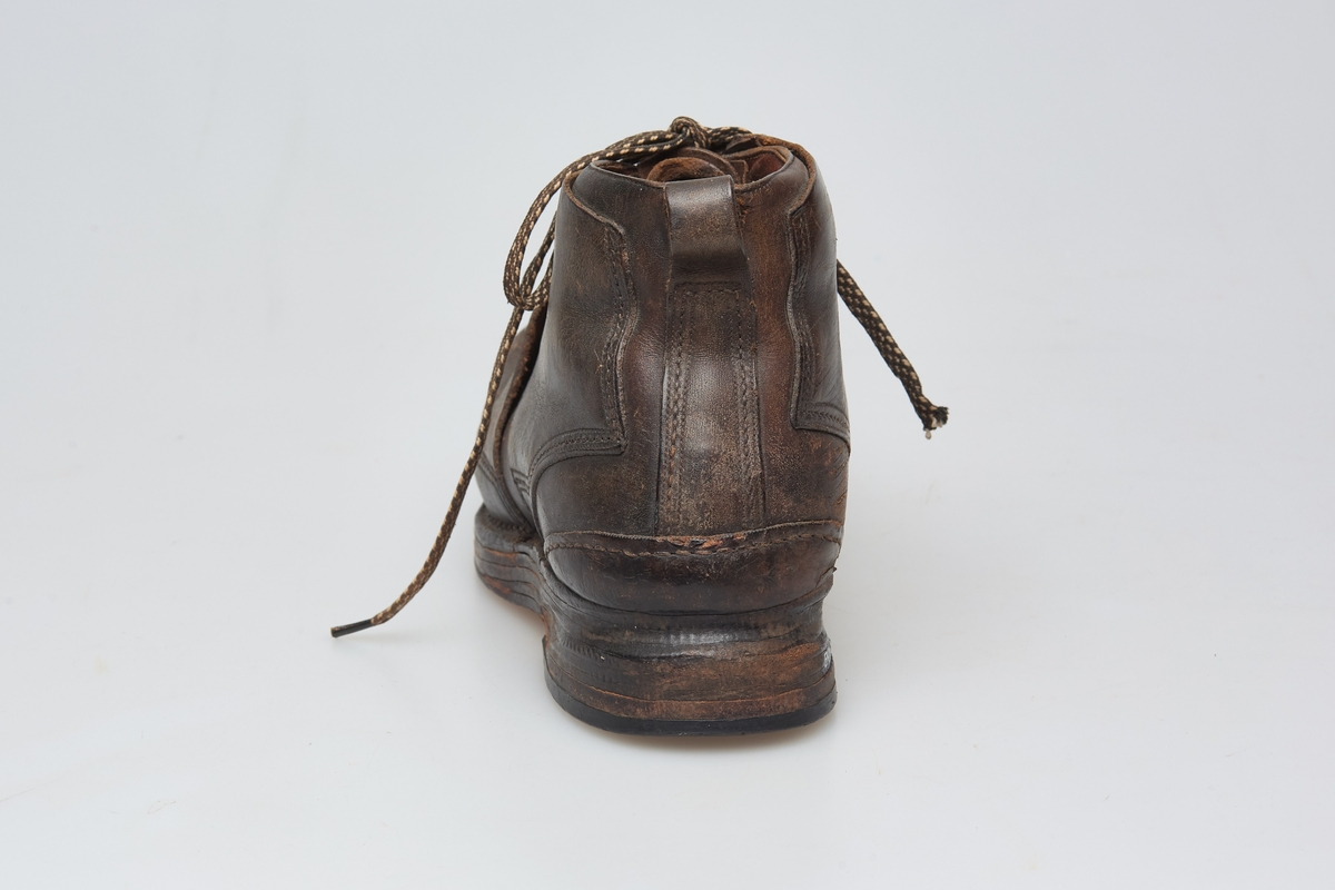 En skisko av brunt lær. Indre tunge og snøring gjennom maljer og hekter med skolisser. Overlappende lag med snøring utenpå dette, med hekter. Såle av lær.