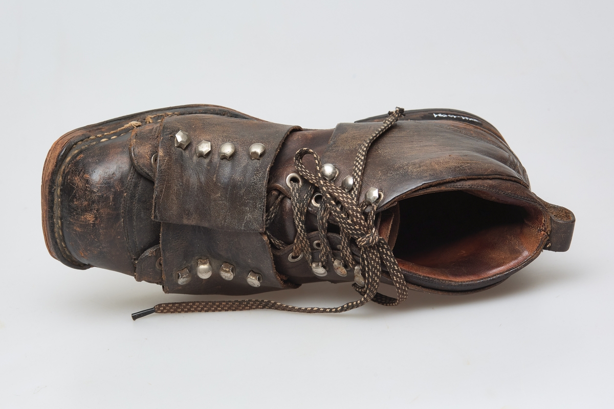 En skisko av brunt lær. Indre tunge og snøring gjennom maljer og hekter med skolisser. Overlappende lag med snøring utenpå dette, med hekter. Såle av lær.