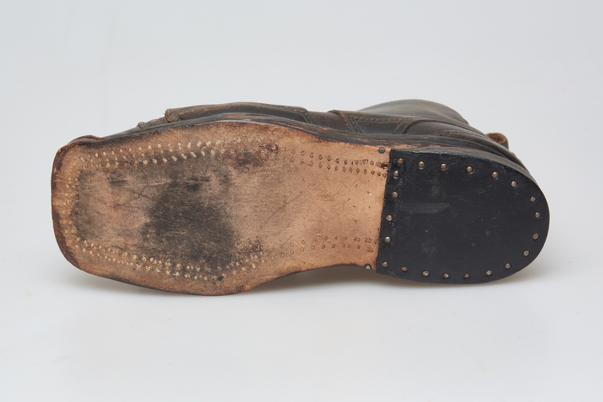 En skisko av brunt lær. Indre tunge og snøring gjennom maljer og hekter med skolisser. Overlappende lag med snøring utenpå dette, med hekter. Såle av lær.