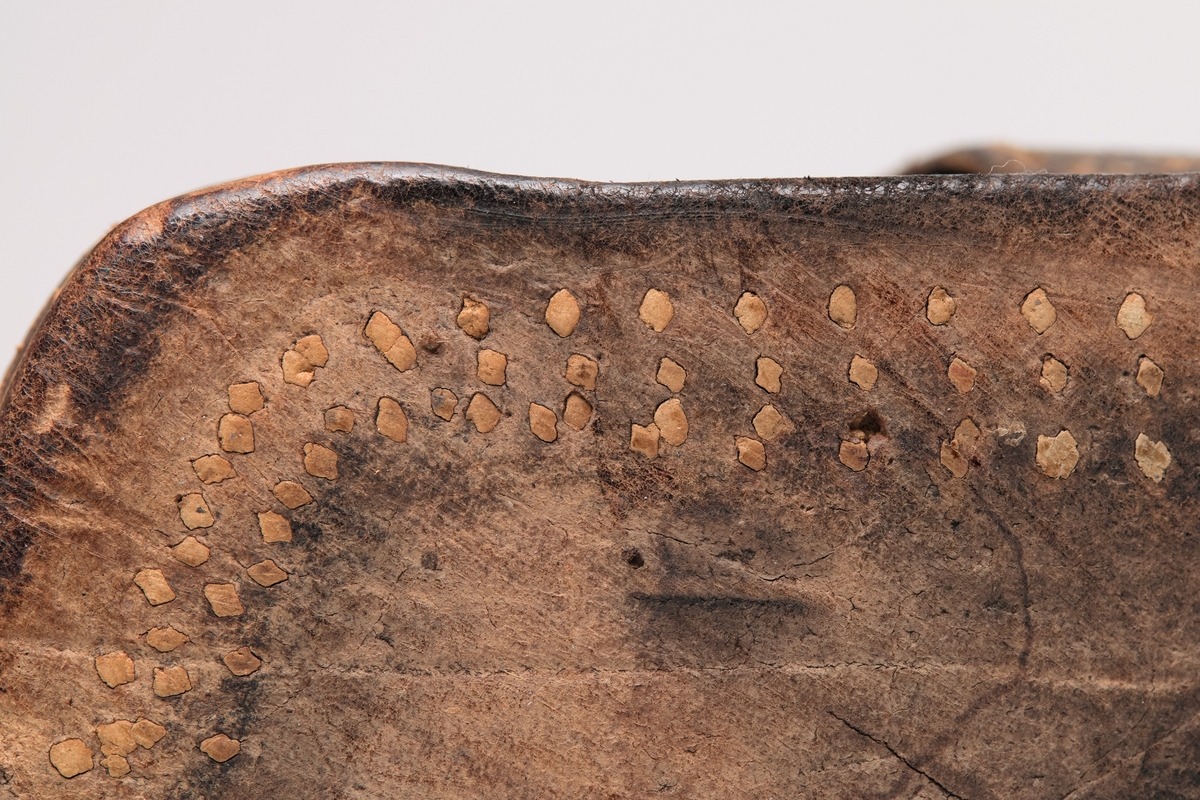 En skisko av brunt lær. Indre tunge og snøring gjennom maljer og hekter med skolisser. Overlappende lag med snøring utenpå dette, med hekter. Såle av lær.