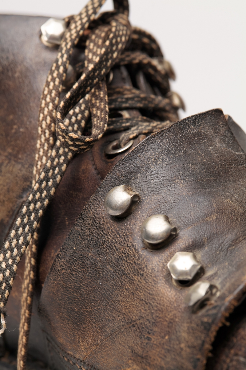 En skisko av brunt lær. Indre tunge og snøring gjennom maljer og hekter med skolisser. Overlappende lag med snøring utenpå dette, med hekter. Såle av lær.