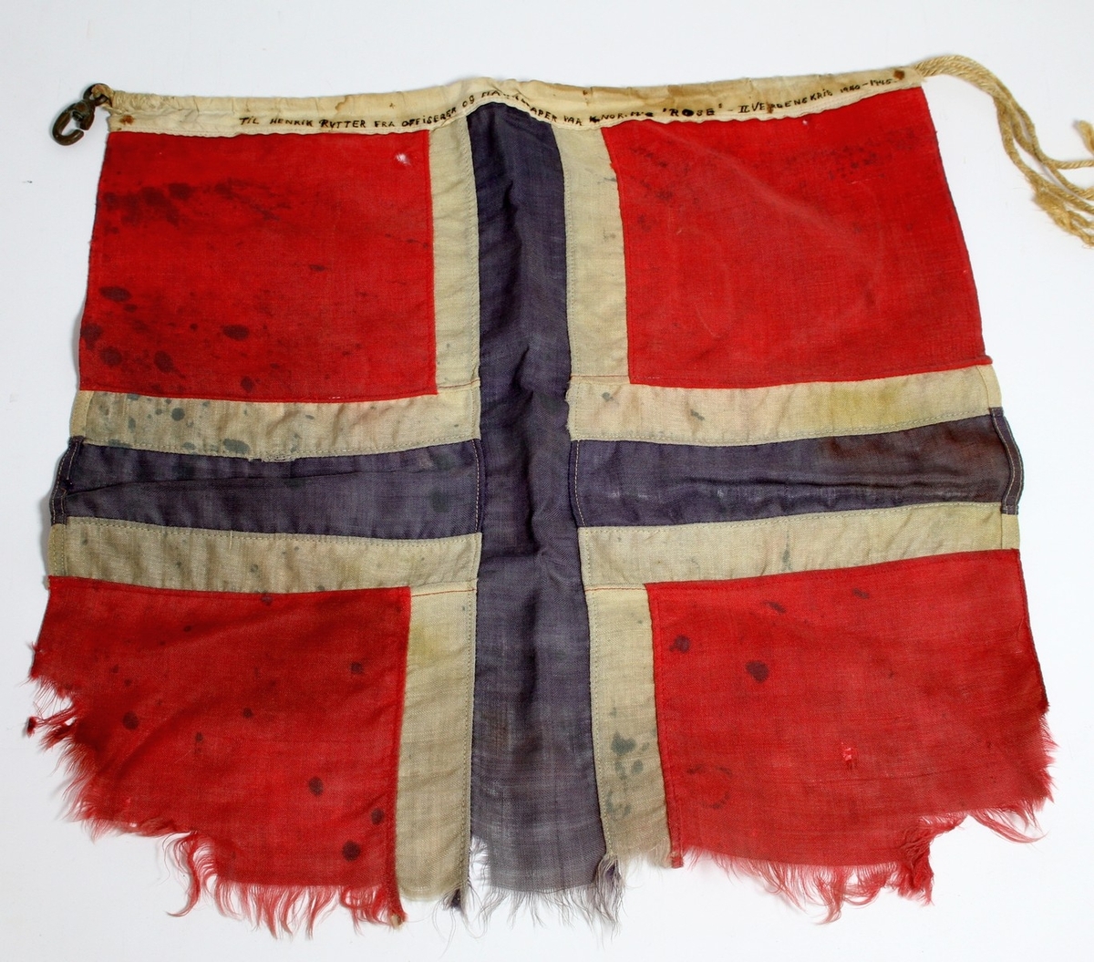 Norsk skipsflagg frå den andre verdskrigen, som vart gjeve i gåve til diktaren Henrik Rytter frå offiserar og mannskap på korvetten H.Nor MS "Rose". Marineskipet "Rose" forliste 26. oktober 1944 etter ein kollisjon med den britiske fregatten Manners. (1) Henrik Rytter var i tysk fangenskap under krigen. 

I den innramma følgjeteksten står det følgjande: "Dette er eit sokalla KAMPFLAGG frå korvetten KNM's "ROSE" som under krigen 1940-1945 var med å lose forsynings-konvoiar i Nordsjøen og Atlanteren. Under eit slikt tokt frå England til New Foundland var Olav Rytter med på reportasje for NRK i London. Nestkommanderande ombord, løytnant Nielsen, kom då med flagget og bad han overlevere det som gåve til far sin, Henrik Rytter, som Nielsen hadde høyrt halde foredrag ein gong i sin ungdom. - Soleis kom flagget til "Rytterhaugen" og Ustedalen, her det no skal bli verande. - 

Den Kgl. Norske Marine hadde fleire slike armerte korvettar i konvoi-fart, og alle hadde blomsternavn, "Rose", "Acantus", "Potentilla" og fleire. Nokre gjekk ned i kamp mot dei tyske ubåtane i Nordsjøen og Atlanteren. Men dei gjorde det nok ogso vanskeleg for fienden sin. Når ein av dei hadde gjort det av med ein tysk ubåt, vart flagget ombord firt ned og teke vare på. -

Eit slikt "kampflagg" er soleis dette flagget, storm-slete og oljeflekkete, men enno friskt i fargane.

Kjelde:
https://www.sjohistorie.no/no/skip/24393/ (Lesedato: 08.12.2020)