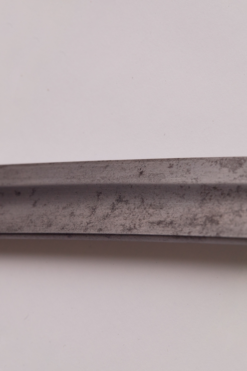 Sabel a): Klingen hulslipt til 17,5 cm fra spissen. Ryggen er tynnslipt fra spissen og 17 cm. oppover. Grepets plate, bøyle og knapp er støpt av messing. Kavlen er av presset horn med rifler hvori metallbånd. Dekorert.