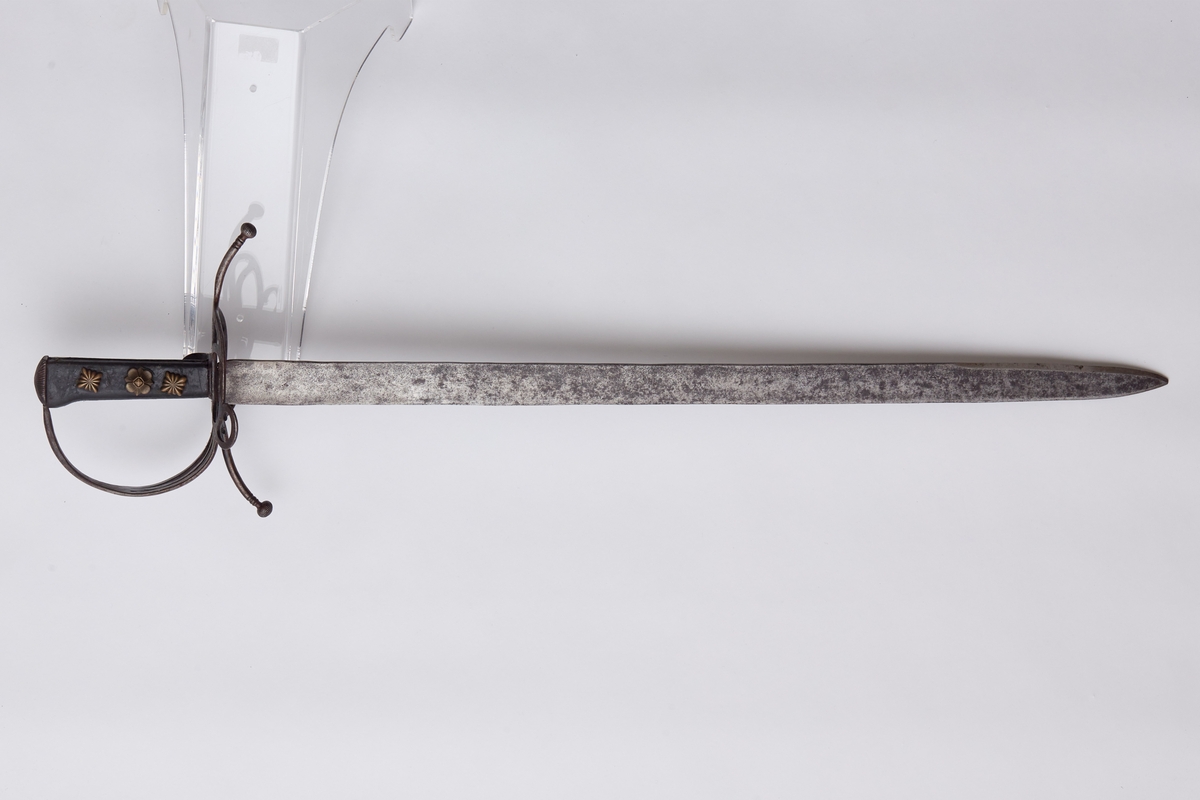 Sabel a): Klingen hulslipt til 17,5 cm fra spissen. Ryggen er tynnslipt fra spissen og 17 cm. oppover. Grepets plate, bøyle og knapp er støpt av messing. Kavlen er av presset horn med rifler hvori metallbånd. Dekorert.